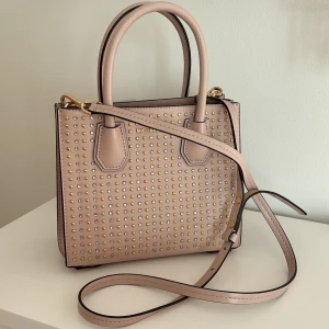 Ljusrosa väska från Michael Kors. - Jättesöt väska från märket Michael kors med fint strass på framsidan av väskan. Man får plats med te.x  mobiltelefon, korthållare, hörlurar och läppglans i väskan. Är i jättefint skick och knappt använd.  