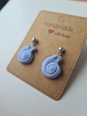 Handgjorda ljusblå snäckörhängen på kulstift - Unika snäckformade/fossilformade handgjorda örhängen i ljusblå färg med silvriga kulstift. Gjorda för hand av mig i polymerlera. 