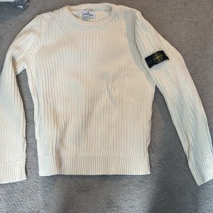 Vit stickad tröja från Stone Island - Säljer en stilren vit stickad tröja från Stone Island med klassisk patch på vänster ärm. Tröjan har rund halsringning, ribbstickade muddar och är tillverkad i ett mjukt material som passar perfekt till lager-på-lager. Enkel men snygg design. Säljer den eftersom jag har växt ut den och tycker den förtjänar nån ny person som kommer trivas i den.