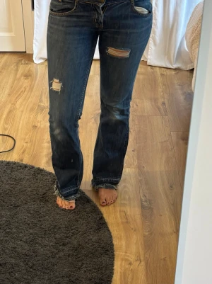 Låga Lee jeans - Lee jeans med låg midja. Har själv gjort revor på dem samt ”förlängt” dem med hjälp av annat jeans material.  Midjemått 37cm Innerbenslängd 79cm