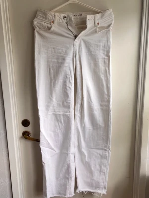 Vita raka jeans med rå kant - Säljer ett par vita jeans med rak passform och rå, fransig kant nedtill. Jeansen har klassisk femficksdesign och hög midja. Perfekta för dig som vill ha en clean look med lite edge.