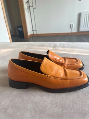 Orange loafers från Vagabond - Säljer ett par snygga orange loafers från Vagabond. Skorna är i slätt läder med klassisk design, låg klack och svarta sulor. Perfekta för dig som vill sticka ut med färg och ändå ha en stilren look.