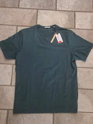 Mörkgrön t-shirt från Bläck - En stilren mörkgrön t-shirt från Bläck i mjuk bomull. Klassisk rund halsringning och korta ärmar. Perfekt basplagg till garderoben och enkel att matcha med olika stilar.
