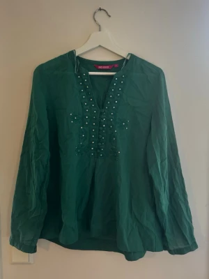 Grön blus med broderi från Indiska - Grön blus från Indiska med långa ärmar, dekorativa knappar framtill och broderade detaljer med små paljetter. Tillverkad i ett tunt, luftigt tyg som ger en avslappnad känsla. Perfekt för dig som gillar boho-vibbar och unika detaljer eller som en tröja man drar på innan stranden. Pris går att diskutera💕💕