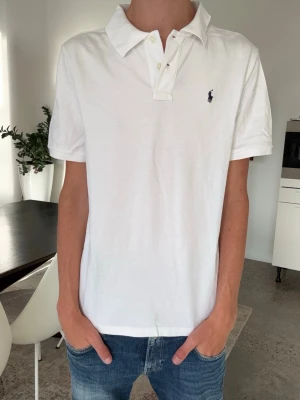 Vit piké från Ralph Lauren - Klassisk vit pikétröja från Ralph Lauren med korta ärmar och krage. Tröjan har knappar vid halsen och den ikoniska lilla loggan broderad på bröstet. Tillverkad i mjuk bomull för en skön känsla och clean look. Barn XL 18-20 passar vanlig S