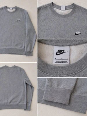Grå crewneck sweatshirt från Nike - Klassisk grå sweatshirt från Nike med broderad svart logga på bröstet. Tröjan har rund halsringning, ribbade muddar vid ärmslut och nederkant samt mjuk insida. Perfekt för en avslappnad och sportig stil.