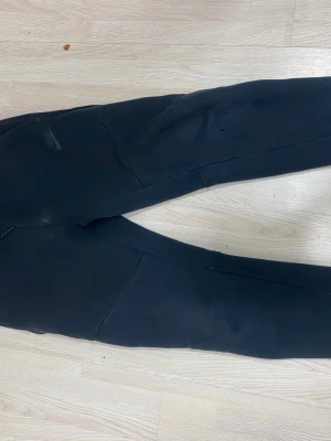 Svarta mjukisbyxor från Nike - Säljer ett par svarta mjukisbyxor från Nike i storlek M. Byxorna har en klassisk rak passform och är tillverkade i mjukt och bekvämt material. Perfekta för chill dagar eller träning. Diskret Nike-logga och elastisk midja för extra komfort.