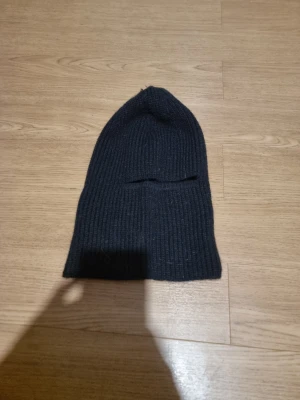 Svart ribbstickad balaklava - INSTABOX!!! En enkel och stilren svart ribbstickad balaklava i klassisk modell. balaklavan  är lång och har en mjuk, stretchig passform som sitter skönt på huvudet. Perfekt för kalla dagar och passar till de flesta outfits.