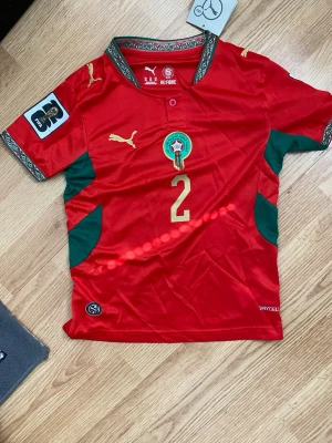 Marocko VM 2026 Hemmatröja - Marocko VM 2026 Hemmatröja med Hakimi namn. Är fint och är oanvänt. Passar bra för 6-8 åringar. Priset kan diskuteras. För frågor skriv bara.  l:I KØPlÂ