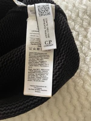 Svart hoodie från C.P. Company - Säljer en svart hoodie från C.P. Company i 100% bomull. Stickad struktur med klassisk huva och diskret logga på insidan. Perfekt för dig som gillar streetwear och vill ha något stilrent men ändå bekvämt.