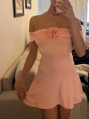 Ljusrosa offshoulder kortklänning - Supersöt ljusrosa kortklänning med offshoulder-design och en dekorativ rosdetalj framtill.  Storlek XS, jag är 1.65cm lång. 