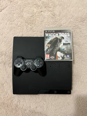PlayStation 3 Slim med kontroll och spel - Säljer en svart PlayStation 3 Slim med en matchande svart DualShock 3-kontroll och spelet Watch Dogs. Konsolen har en stilren, matt finish och klassisk PS3-design. Perfekt för dig som vill spela klassiska PS3-titlar och njuta av en riktig gamingupplevelse.