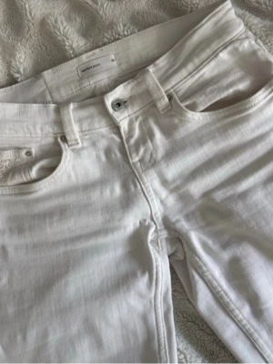 Vita utsvängda jeans med låg midja - Snygga vita jeans med utsvängda ben och låg midja. Klassisk femficksmodell med bälteshällor och dragkedja. Perfekta för en fräsch och trendig look, passar till allt och är lätta att styla. Materialet är denim med lite stretch för extra komfort.