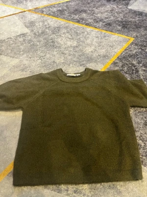 Olivgrön stickad tröja 157 - Olivgrön stickad tröja från 157 med rund halsringning och ribbade muddar. Tröjan har en enkel och stilren design, perfekt för lager på lager och passar till många olika outfits. Materialet känns mjukt och bekvämt.