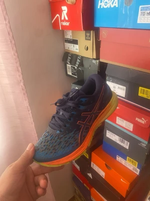 ASICS DynaFlyte 4  - Säljer ett par snygga blå löparskor från Asics med orange och gul sula. Ovandelen är i mesh för bra ventilation och skorna har klassisk Asics-logga på sidan. Perfekta för löpning eller träning och ger bra stöd och komfort.