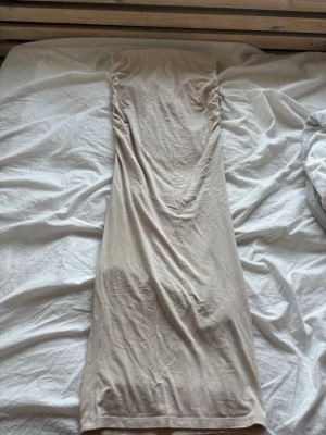 Beige långklänning med rynkade sidor - Säljer en beige långklänning i mjukt material med rynkade detaljer längs sidorna. Klänningen har en enkel, rak passform och är perfekt för dig som gillar minimalistisk stil. Passar till många olika tillfällen och är lätt att styla med accessoarer. Aldrig använd och så gott som ny. Är en del av ett set med ett linne som jag också säljer. Vid köp av båda 249 kr. Nypris på kjolen 300 kr, mitt pris 199 kr. 