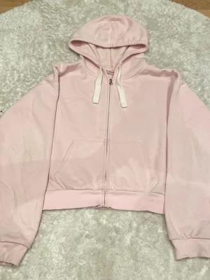 Ljusrosa hoodie med dragkedja Gina Tricot - Ljusrosa hoodie från Gina Tricot i storlek M. Hoodien har dragkedja framtill, stora fickor och vita snören i huvan. Tillverkad i mjukt material med ribbade muddar vid ärmar och nederkant. Perfekt för en chill och avslappnad stil.