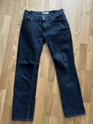 Svarta raka jeans - Säljer ett par svarta jeans med rak passform och klassisk femficksdesign. Jeansen har silverfärgade nitar och knapp, samt kontrastsömmar. Perfekta för dig som gillar en enkel och stilren look.