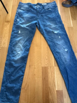 Blå slitna jeans från Hugo Boss - Dom är lite smutsiga men det går att tvätta bortSäljer ett par blå jeans från Hugo Boss med slitna detaljer och tvättad look. Jeansen har klassisk femficksmodell och raka ben. Materialet är mjukt denim som ger en avslappnad vibe. Perfekta för dig som gillar en trendig och casual stil.