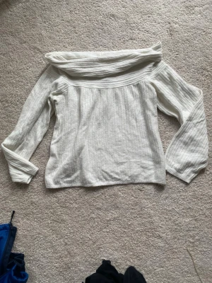 Vit off shoulder stickad tröja - Säljer en vit stickad tröja med off shoulder-design och bred krage. Tröjan har långa ärmar och är ribbstickad vilket ger en snygg struktur. Perfekt för dig som vill ha en stilren och trendig look.