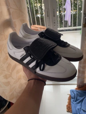 Adidas Samba vita sneakers - Adidas Samba LT sneakers i vitt läder med svarta detaljer och gummisula. Skorna har svarta ränder på sidorna, svart plös och breda svarta skosnören. Tidlös retrostil med låg profil och tydlig Adidas-logga på plösen. Skorna var för stora för mig när jag köpte de. Om ni har några frågor så svarar jag gärna.