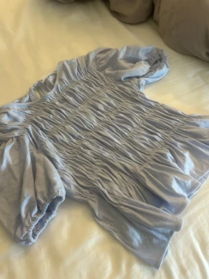 Ljuslila blus med puffärm och rynk - Supersöt ljuslila blus med puffärmar och rynkdetaljer över hela framsidan. 