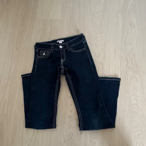 Mörkblå bootcut jeans med kontrastsömmar - Snygga mörkblå bootcut jeans med vita kontrastsömmar och dekorativa ficklock bak. Klassisk femficksmodell med knapp och dragkedja framtill. Jeansen har en tidlös look och passar perfekt till en avslappnad stil.