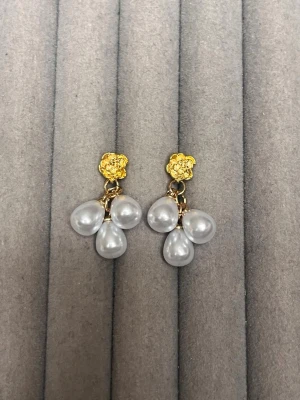 Guldörhängen med droppformade pärlor - Säljer ett par eleganta örhängen med guldfärgade detaljer och tre droppformade vita pärlor på varje örhänge. Örhängena har en unik, lite skulptural guldfärgad platta vid fästet och pärlorna hänger i klasar. Perfekt accessoar för att lyfta din stil.