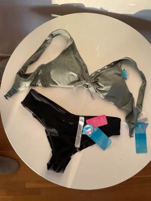 Ribbad bikini i grönt och svart, hipsters, stl M-L - Snygg bikini med ribbad grön överdel som har knyt framtill och dekorativa knappar. Svarta bikiniunderdelar i enkel design. Perfekt för stranden eller poolen. Båda delarna har tags kvar. Överdel- stl M, underdel - stl L 