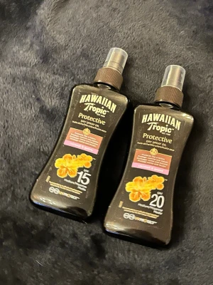 Hawaiian Tropic sololja SPF 15 & 20 - Två flaskor Hawaiian Tropic Protective Dry Spray Oil, en med SPF 15 och en med SPF 20. Båda är 200 ml och har en brun plastflaska med sprayfunktion och tropisk doft. Perfekt för dig som vill ha skydd och glansig hud på stranden.