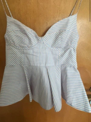 Topp  - Snygg topp med tunna axelband och bystdetalj. Toppen har ett blått och vitt randigt mönster och en lätt utsvängd nederdel. Perfekt för varma dagar och enkel att styla till jeans eller kjol.