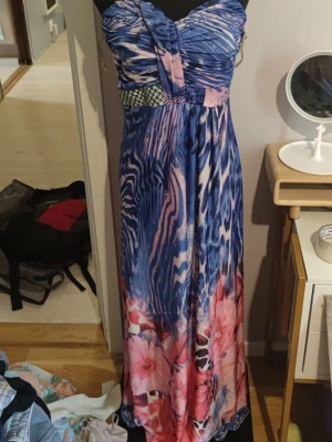 Färgglad maxiklänning med halterneck  - Säljer en jättefin, golvlång maxiklänning i ett stretchigt och skönt material! Klänningen har ett unikt mönster i blått, lila och rosa med en blandning av djurinspirerade ränder och blommor. Detalj med fint mönstrat band under bysten och smickrande drapering.Storlek: Ingen lapp kvar, men uppskattas passa som S–M