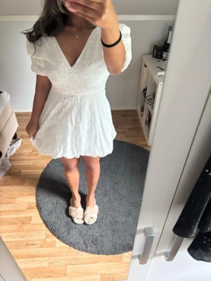 Vit kort klänning med broderi - Superfin vit kort klänning med v-ringning och broderade blommor. Klänningen har puffiga korta ärmar och en lätt utställd kjol. Perfekt för sommarens alla tillfällen. Tänkt att användas som student klänning!
