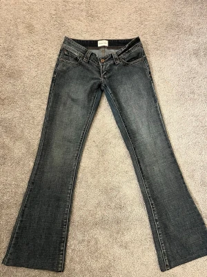 Bootcut jeans i mörk denim - Säljer ett par snygga bootcut jeans i mörkblå denim med klassisk femficksdesign och låg midja. Jeansen har subtila slitningar och vida ben som ger en retrovibe. Perfekta till sneakers eller boots för en avslappnad look.