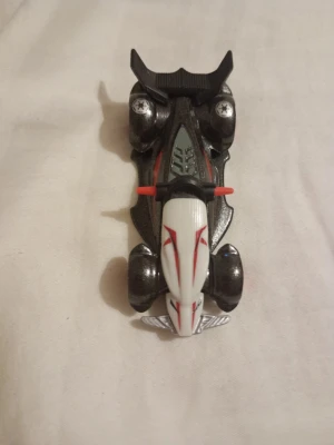 Hotwheels i metall - En cool leksaksbil i svart och vitt med röda detaljer och stora bakvinge. Bilen har röda fälgar, silverfärgade dekaler och sportig design. Perfekt för dig som gillar samlarbilar eller vill ha något snyggt till hyllan.                 