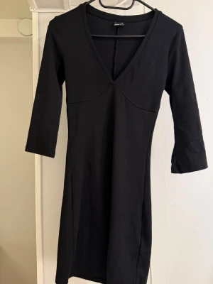 Svart v-ringad klänning med trekvartsärm  - En svart klänning med v-ringning och trekvartsärm. Klänningen har en enkel, figurnära passform och är tillverkad i ett mjukt material som känns bekvämt mot huden. Perfekt för dig som gillar stilrena plagg med en klassisk siluett.