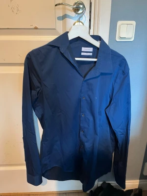 Calvin Klein skjorta - Säljer en snygg marinblå Calvin Klein skjorta då den är för stor för mig, men som passar bra till alla tillfällen. Men skicket är helt nytt i princip. Priset är väldigt bra eftersom nypriset annars är över 1000 lappen!