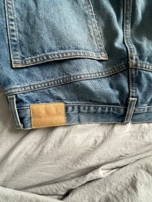 Ljusblå raka jeans med bakfickor - Säljer ett par ljusblå jeans med raka ben och två stora bakfickor. Jeansen har klassisk denimlook och en beige patch bak i midjan. Perfekta för en avslappnad och trendig stil. Materialet är kraftig bomullsdenim.