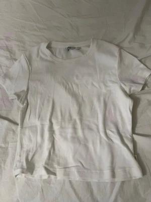 Vit basic t-shirt  - En klassisk vit t-shirt i mjuk bomull. Modellen har rund halsringning och korta ärmar. Passformen är normal och tyget känns lätt och bekvämt mot huden.