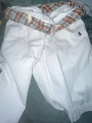 Vita shorts från Polo Ralph Lauren - Snygga vita shorts från Polo Ralph Lauren med klassisk broderad logga på benet. Insidan har ett rutigt foder i orange, grått och vitt. Shortsen har dragsko i midjan och är tillverkade i ett mjukt bomullstyg.