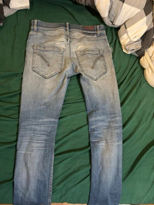 Ljusblå slim fit jeans, storlek 30 - Säljer ett par ljusblå slim fit jeans med klassisk femficksdesign och snygga slitningar baktill. Jeansen har kontrastsömmar och är tillverkade i denim med en skön passform. Perfekta för en avslappnad och trendig look.