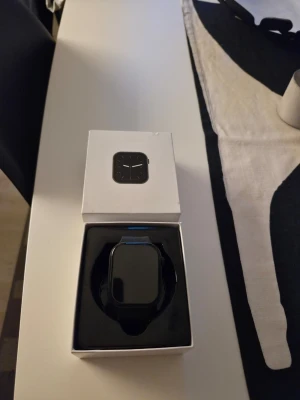 Svart smartklocka i originalförpackning - Stilren svart smartklocka med rektangulär skärm och silikonarmband. Klockan levereras i sin originalförpackning och har en modern, minimalistisk design som passar till de flesta stilar. Perfekt för dig som vill ha koll på notiser och hälsa direkt på handleden.
