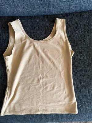 Beige ribbad linnetopp - Säljer en enkel och stilren beige linnetopp i ribbad bomull. Toppen är ärmlös med breda axelband och rundad halsringning. Perfekt att matcha med jeans eller kjol för en clean look.