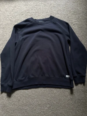 Mörkblå sweatshirt med lång ärm - En enkel och stilren mörkblå sweatshirt med rund hals och långa ärmar. Tröjan har en relaxed passform och ribbade muddar vid ärmslut och nederkant. Perfekt att slänga på sig till jeans eller mjukisbyxor.