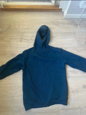 Blå hoodie med strasstryck och dragkedja - Säljer en blå hoodie med huva och dragkedja framtill. På framsidan finns ett stort tryck med texten 'AIM FOR THE MOON' och en tecknad figur samt måne i glittrande strasstenar. Hoodien har fickor framtill och ribbade muddar. Perfekt för dig som gillar statement-plagg.
