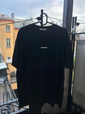 Svart Acne Studios t-shirt - Säljer en svart t-shirt från Acne Studios med klassisk passform och diskret logga på bröstet. T-shirten har rund hals och korta ärmar, perfekt till en enkel och stilren look. Materialet är mjuk bomull som känns skön mot huden.