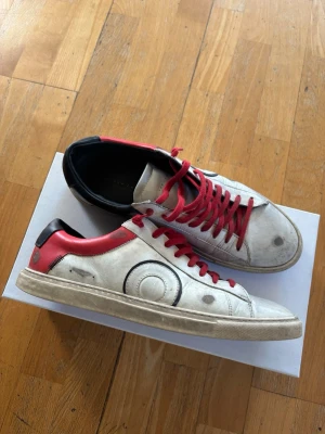 Olivier Cabell  - Tja! Säljer ett par vita sneakers från Olivier cabell med röda skosnören och detaljer i svart och rött på hälen. Klassisk siluett som passar till många olika stilar. Skorna är i bra skick. Säljs då dem inte kommer till användning. Box o dustbag medlommer vid köp. Pris kan diskuteras vid snabb affär💯