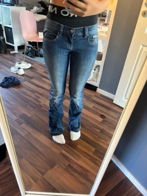 Blå bootcut jeans med kontrastsömmar - Säljer ett par klassiska blå bootcut jeans med snygga kontrastsömmar och femficksmodell. Jeansen har normalhög midja och lätt utsvängda ben. Perfekta till sneakers eller boots och ger en avslappnad men ändå trendig look. Jeansen är upp spreda.