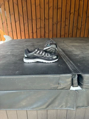 Svarta Nike sneakers med vita detaljer - Säljer ett par svarta Nike sneakers med vita detaljer och reflekterande inslag. Skorna har en sportig design med mesh och syntetmaterial, samt en vit sula som ger bra dämpning. Perfekta för dig som gillar en clean och stilren look.