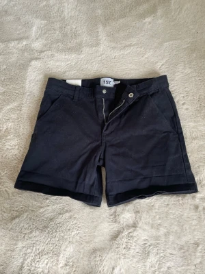 Mörkblå jeanssshorts i storlek 150 från Lager 157 - Snygga mörkblå shorts. Shortsen har fickor fram och bak, bälteshällor och stängs med knapp och dragkedja.